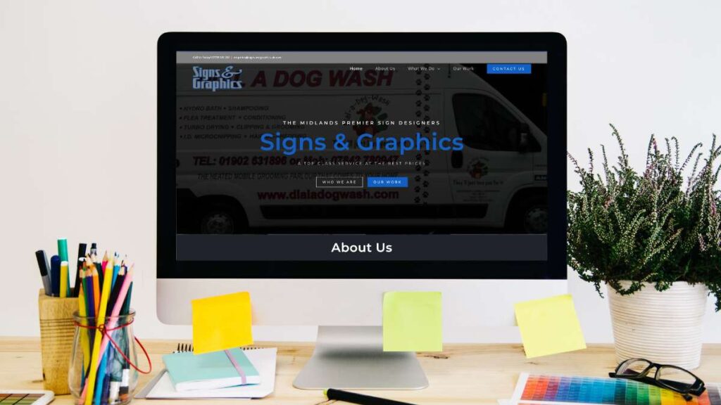 A laptop screen showing the "Signs & Graphics" company website featuring a branded dog wash van.