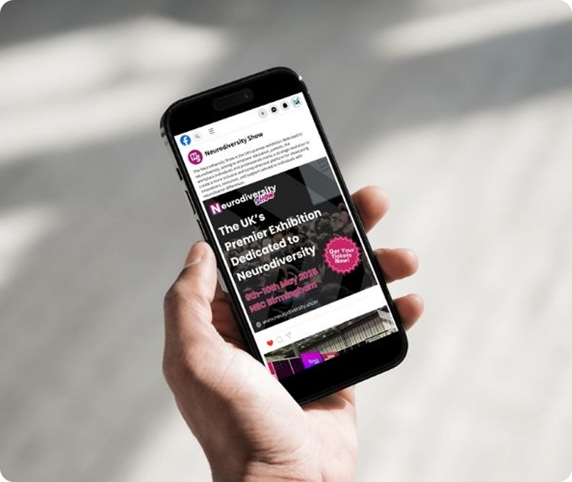 A person's hand holding a smartphone displaying a Facebook post for the Neurodiversity Show, featuring an event advertisement for May 2026 at the NEC Birmingham.