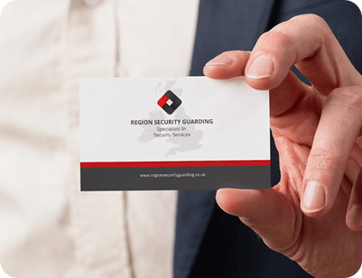 A close-up shot of a person's hand holding a professional white business card for "Region Security Guarding," featuring a red and grey logo and a map silhouette of the UK.