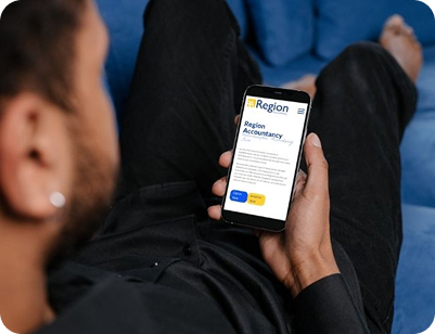 A person sitting on a blue sofa holding a smartphone that displays the mobile website for "Region Accountancy," featuring blue and yellow call-to-action buttons.