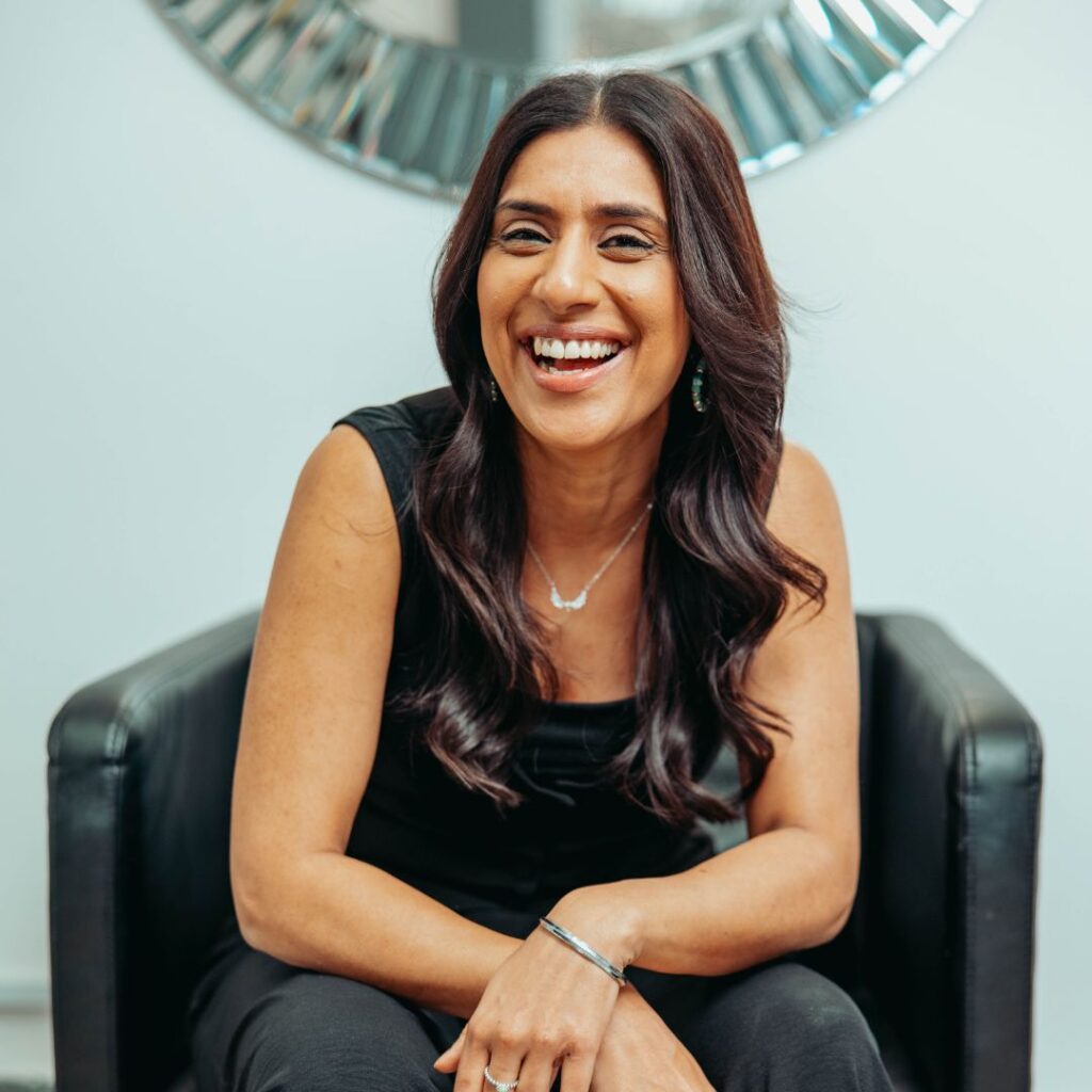 Smiling woman with long dark hair sitting in a chair indoors.