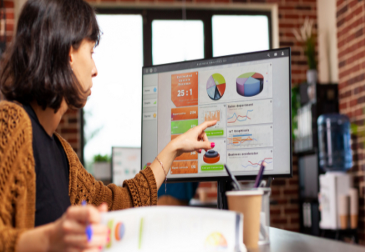 Person pointing at charts and graphs on a computer screen during a data presentation.