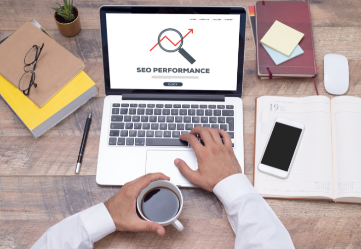 Person working on a laptop displaying SEO performance analytics while holding a cup of coffee at a wooden desk.