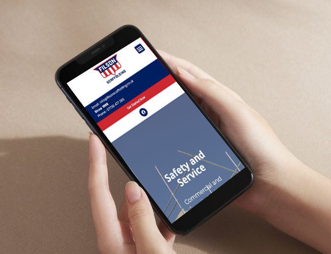 A hand holding a smartphone displaying the mobile website for Filson Scaffolding, featuring a red, white, and blue logo and the slogan "Safety and Service."