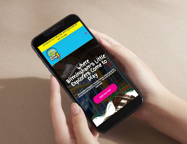 Hands holding a smartphone displaying a children’s play and activity website on the screen.