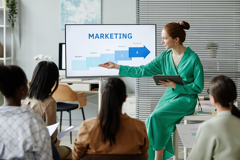 Marketing professional presenting a step-by-step marketing strategy on a screen to a small team during a business meeting.