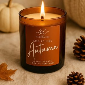 Lit autumn-scented candle in an amber glass jar with pinecones and leaves.