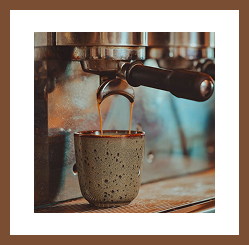 Espresso pouring from a coffee machine into a ceramic cup.