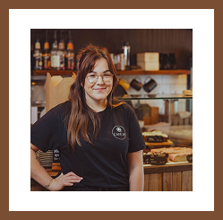 Barista standing behind the café counter, smiling at the camera.