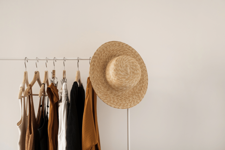 Neutral-toned clothes hanging on a rack with a straw hat.
