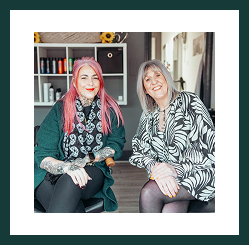 Two women seated together, smiling warmly in a relaxed office setting