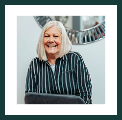 Portrait of a smiling woman with grey hair seated indoors, wearing a striped top