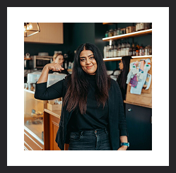 Woman smiling and gesturing in a café or workspace.