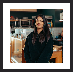 Woman smiling while standing in a café or workspace.