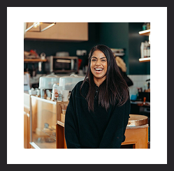 Woman smiling while standing in a café or workspace.