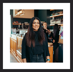 Woman smiling and standing in a café or workspace.